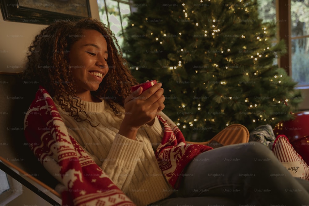 a woman sitting in front of a christmas tree holding a cup