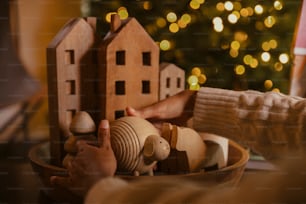 a person holding a wooden toy house in front of a christmas tree