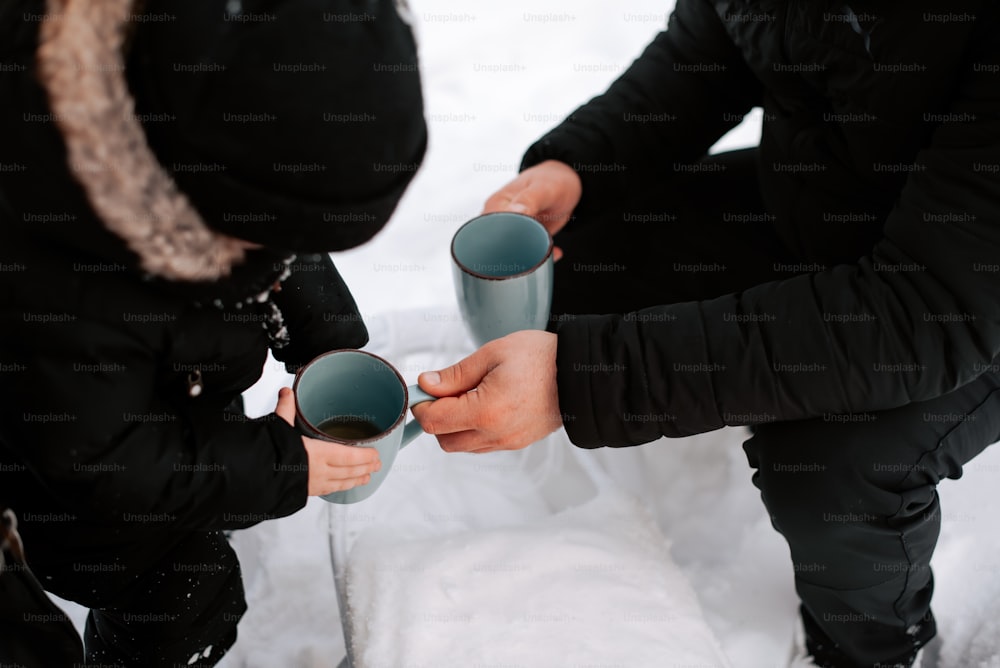 Deux personnes tenant des tasses dans leurs mains dans la neige