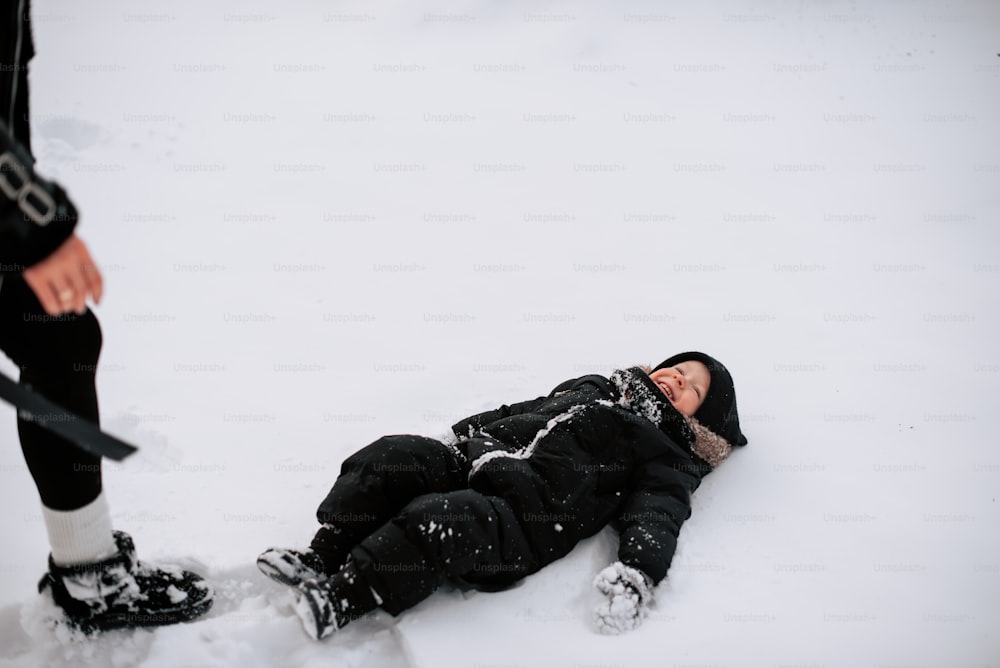 una persona sdraiata sulla neve accanto a una persona con gli sci