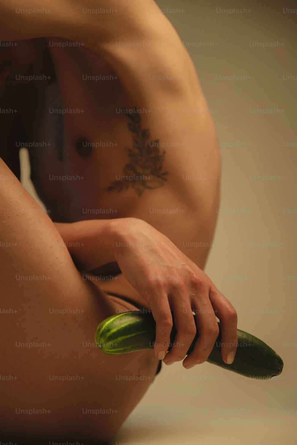 a naked man holding a cucumber in his right hand