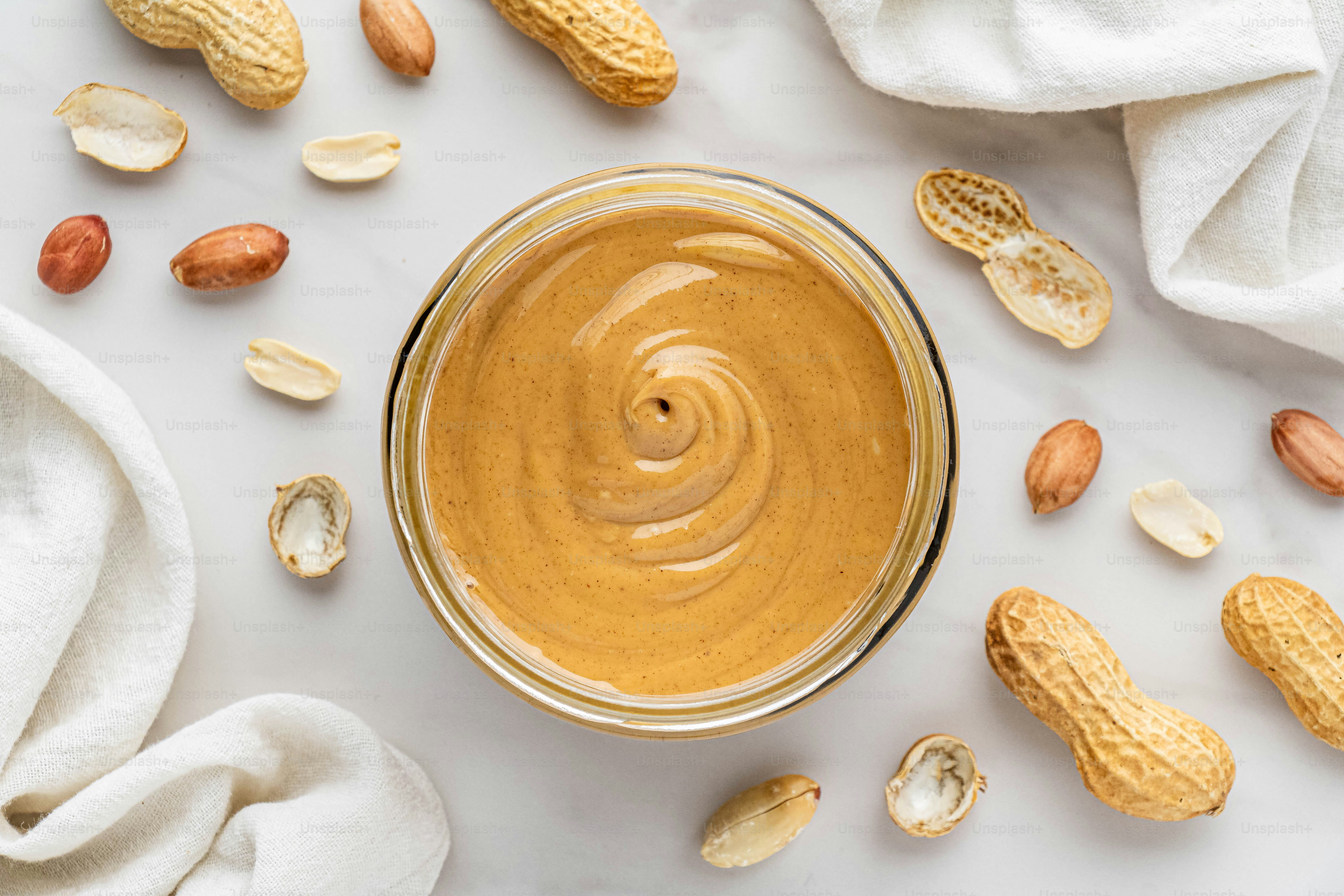 ein Glas Erdnussbutter, umgeben von Erdnüssen