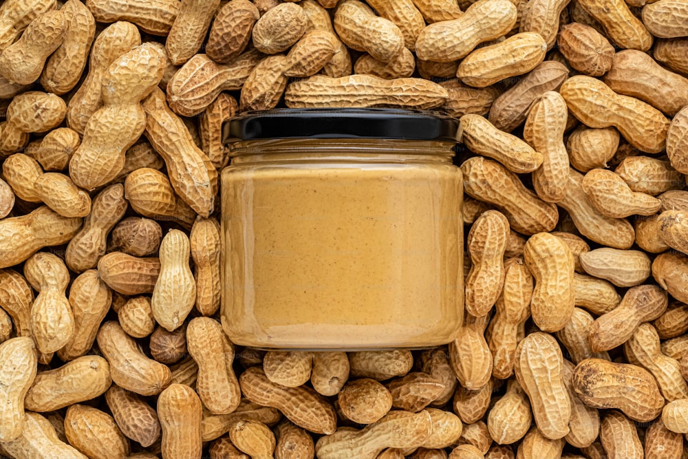 a jar of peanut butter surrounded by peanuts