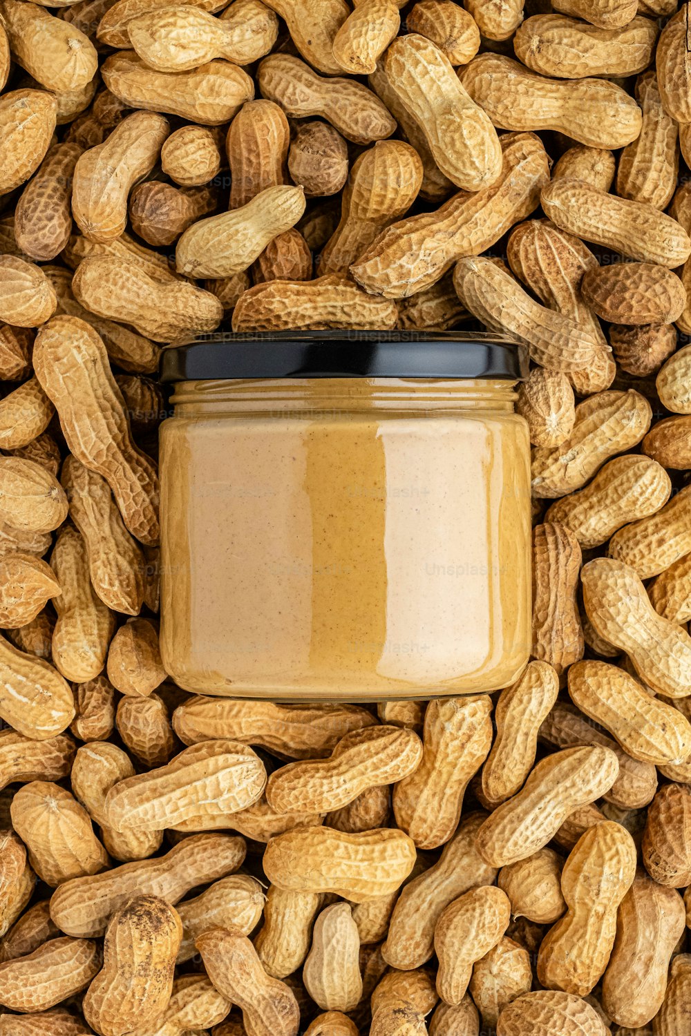 a jar of peanut butter surrounded by peanuts