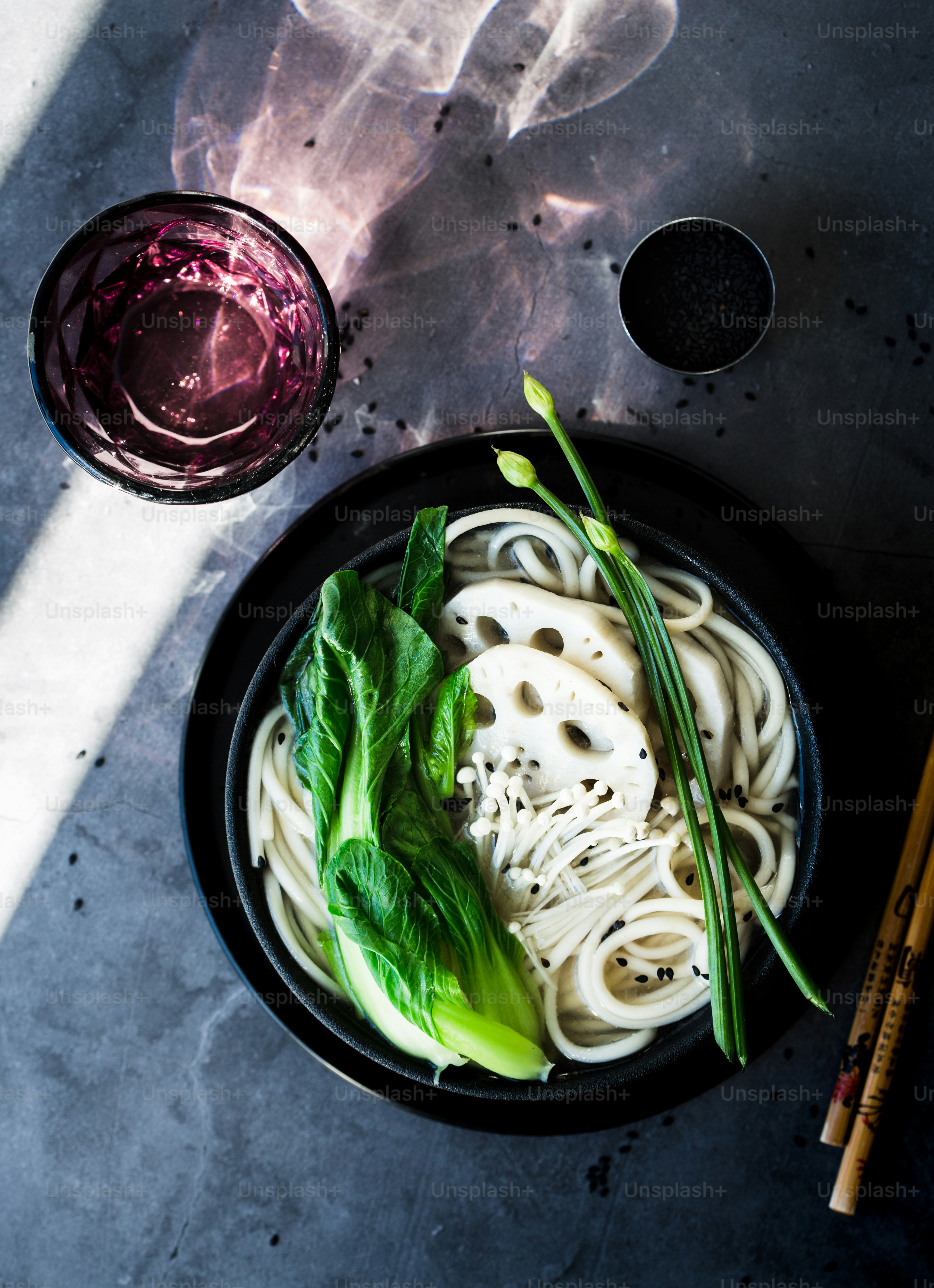 A bowl of noodles and greens next to a glass of wine photo Food Image