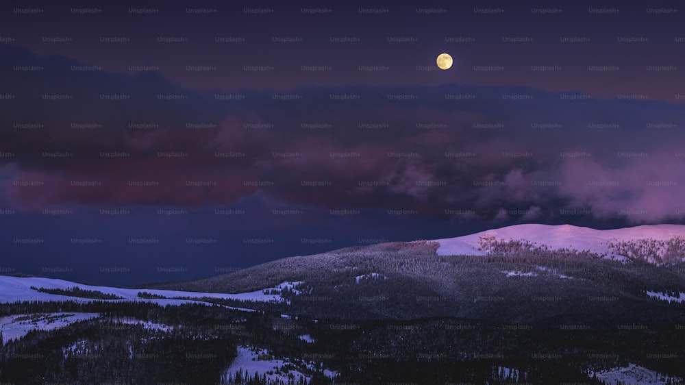 Une pleine lune est vue au-dessus d’une montagne enneigée
