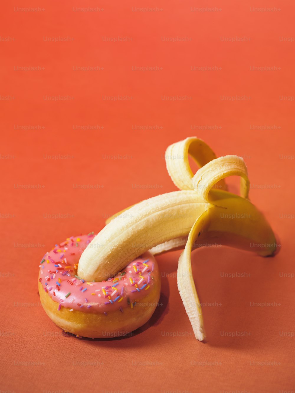 eine Banane und ein Donut mit Streuseln auf rotem Hintergrund