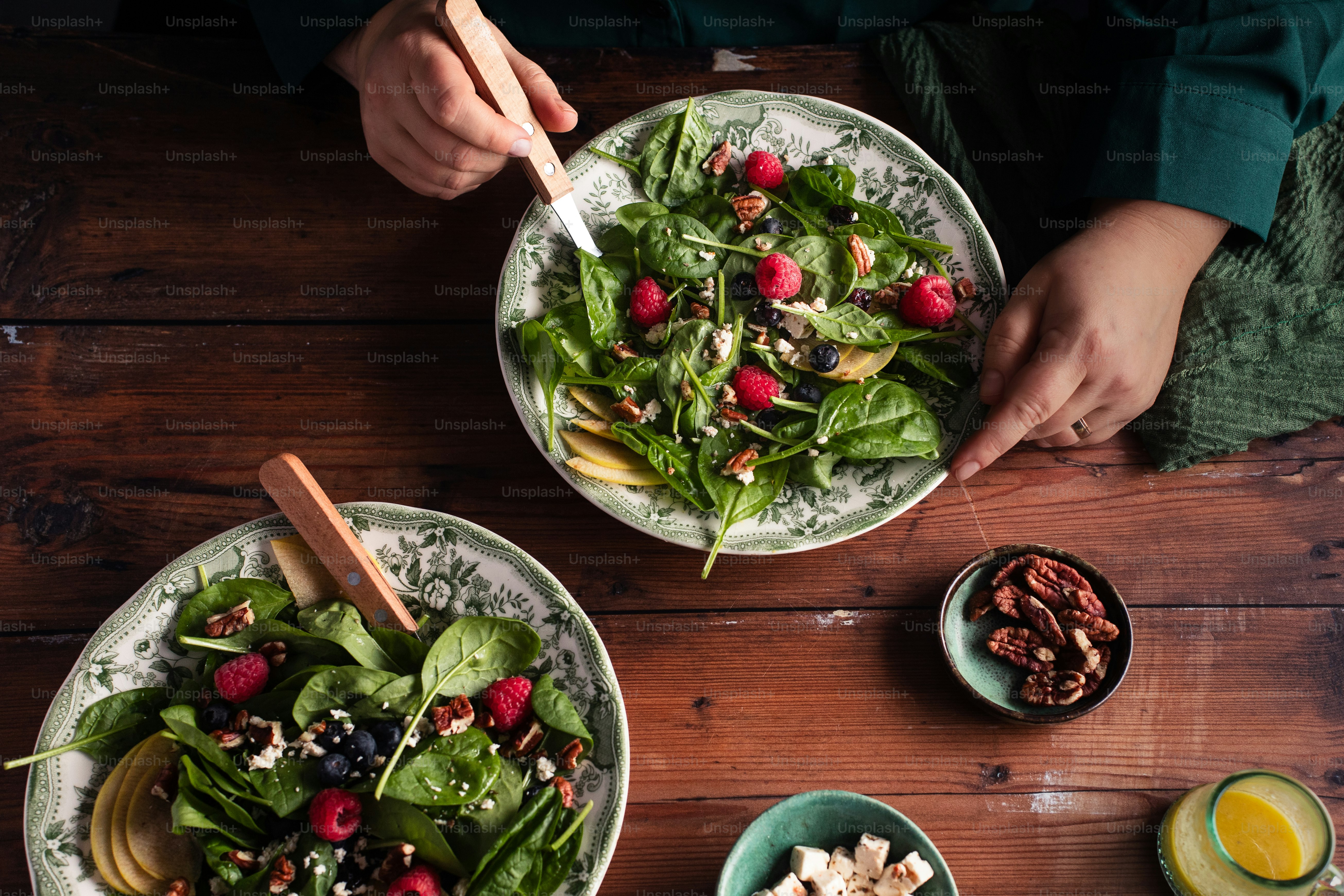 two plates of salad with raspberries and nuts on a wooden table