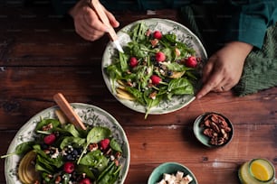 two plates of salad with raspberries and nuts on a wooden table
