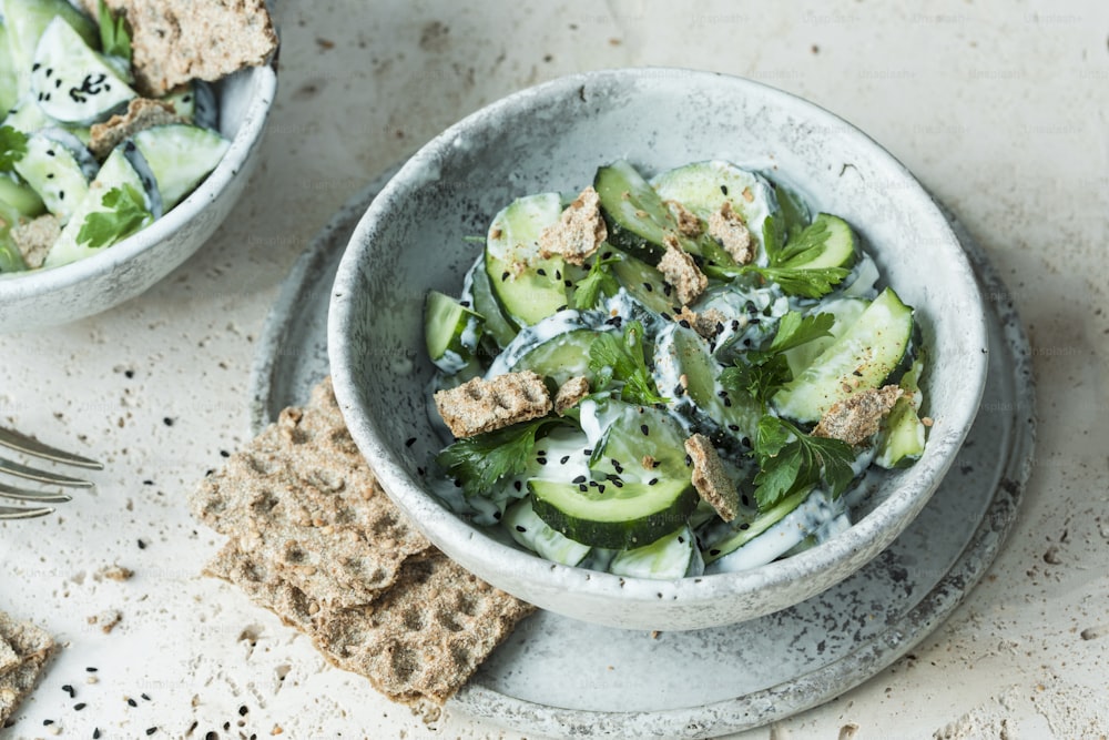 a bowl of cucumber salad with crackers and a fork