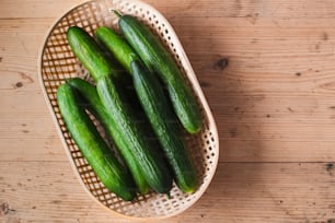 a basket filled with green cucumbers on top of a wooden table