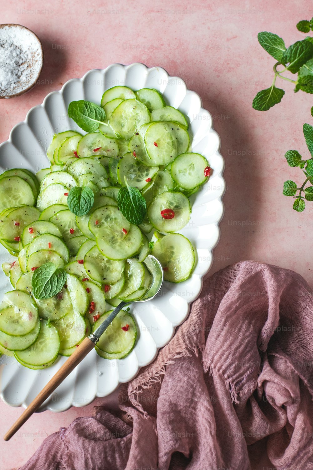 a plate of cucumbers with a spoon on a pink table
