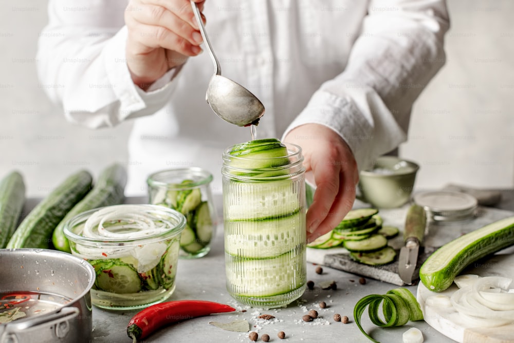 a person is spooning cucumbers into a jar