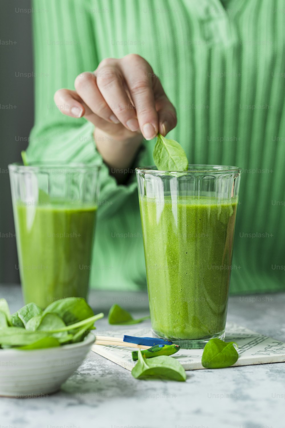 a person putting a leaf in a glass of green smoothie