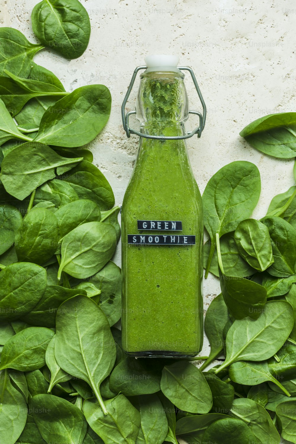 a green smoothie in a glass bottle surrounded by green leaves