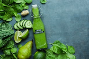 a green smoothie in a bottle surrounded by fruits and vegetables