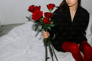 une femme assise sur un lit tenant un bouquet de roses