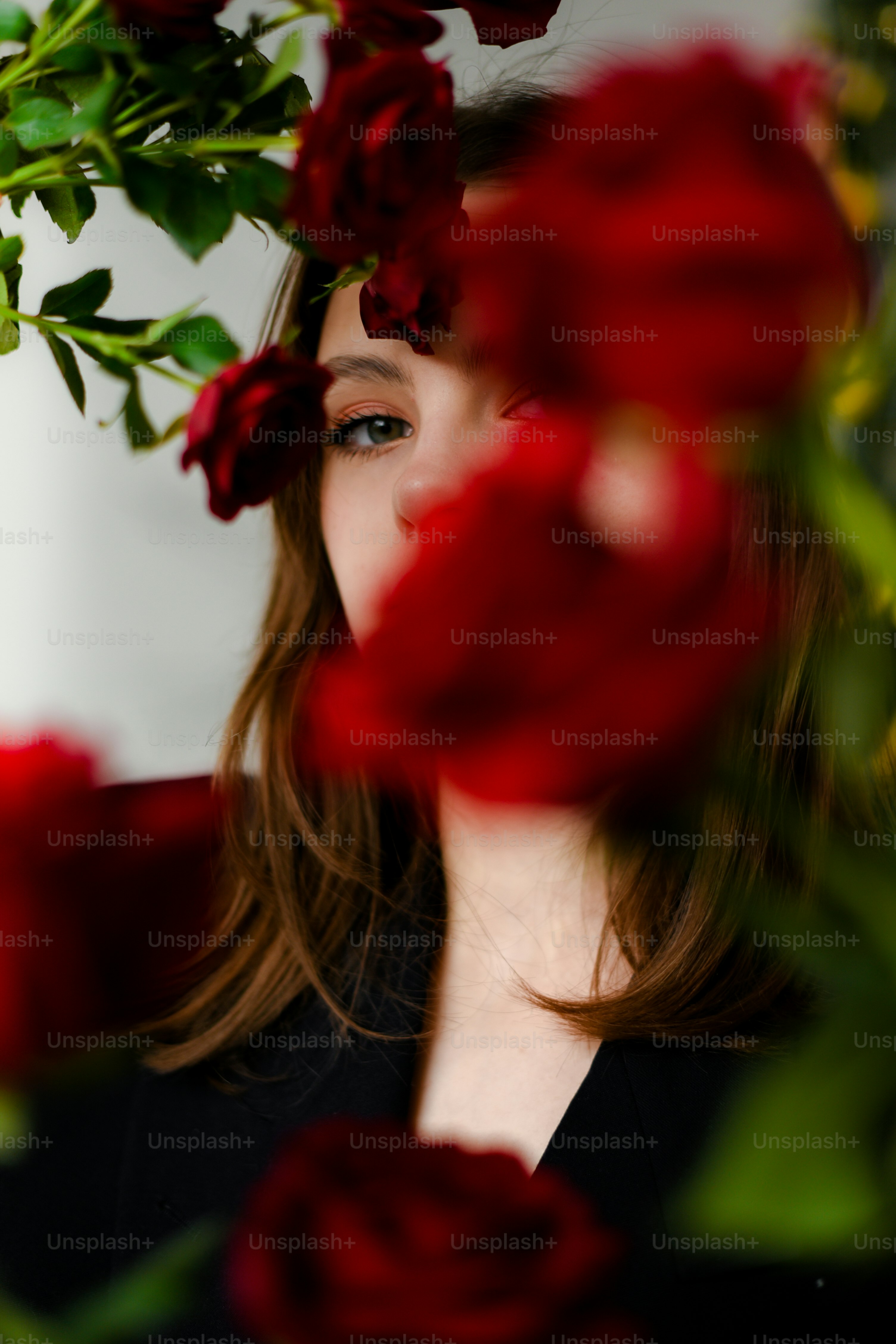 A woman with long hair and a black shirt is surrounded by red roses ...