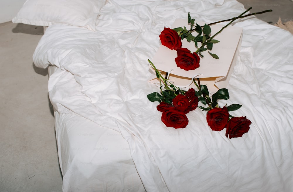 a white bed topped with red roses next to a book