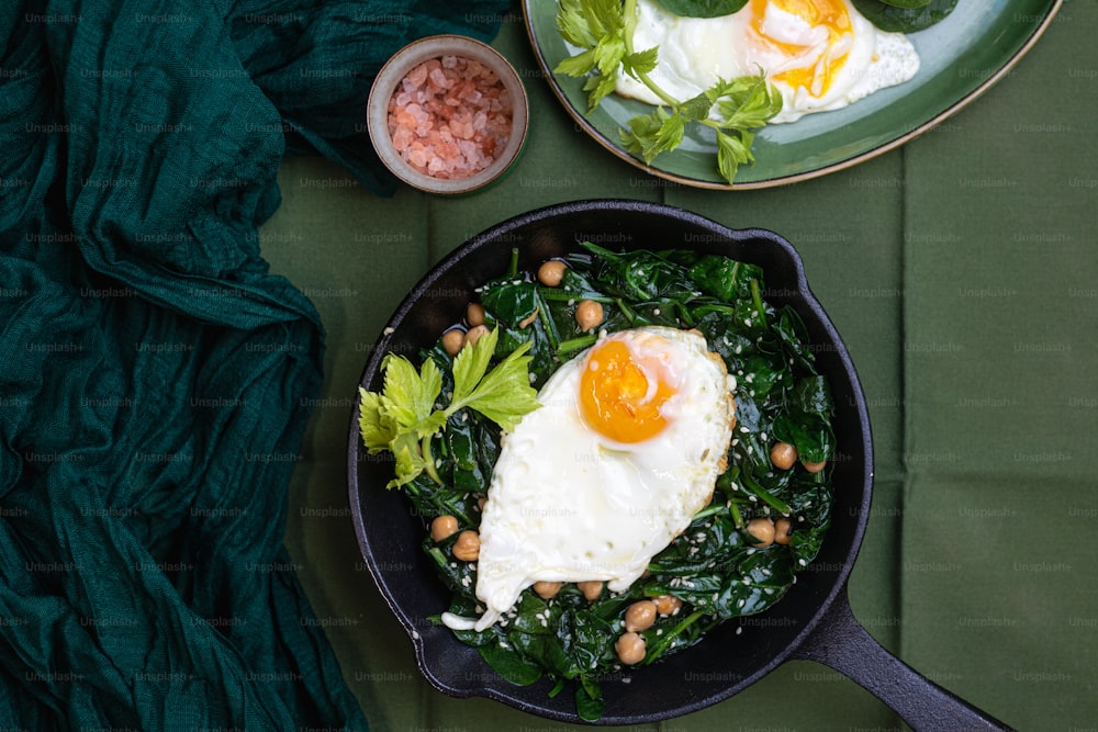 a skillet filled with greens and eggs on top of a table