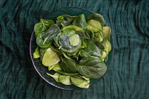 a bowl of spinach leaves on a green cloth