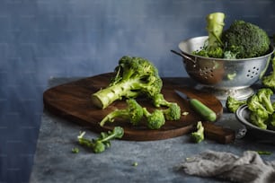 a wooden cutting board topped with broccoli next to a bowl of brocco