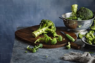 a wooden cutting board topped with broccoli next to a bowl of brocco