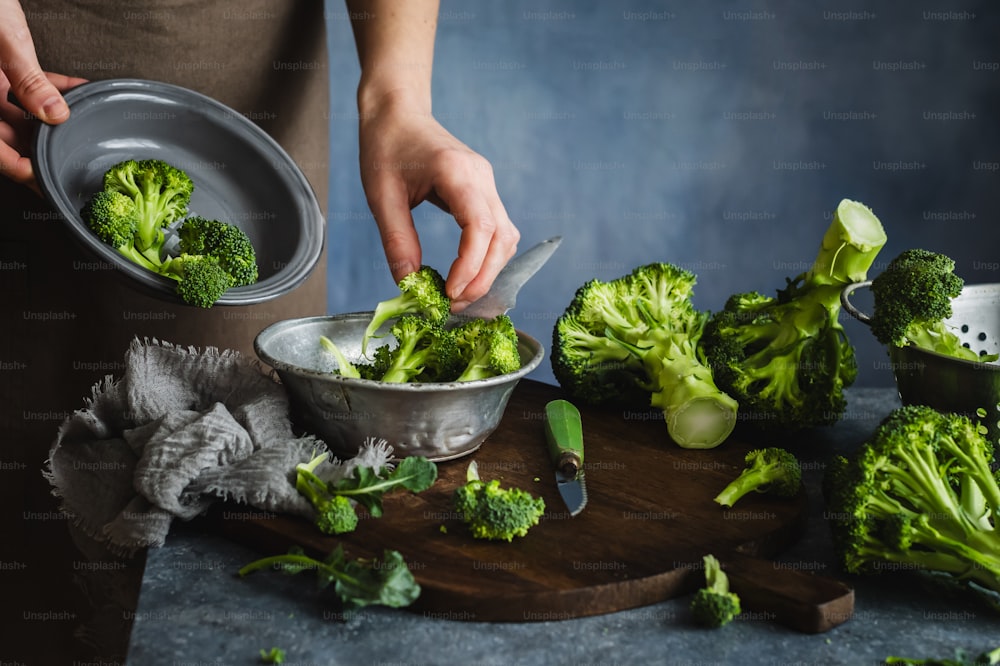 a person cutting broccoli into pieces on a cutting board