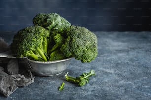 a metal bowl filled with broccoli on top of a table