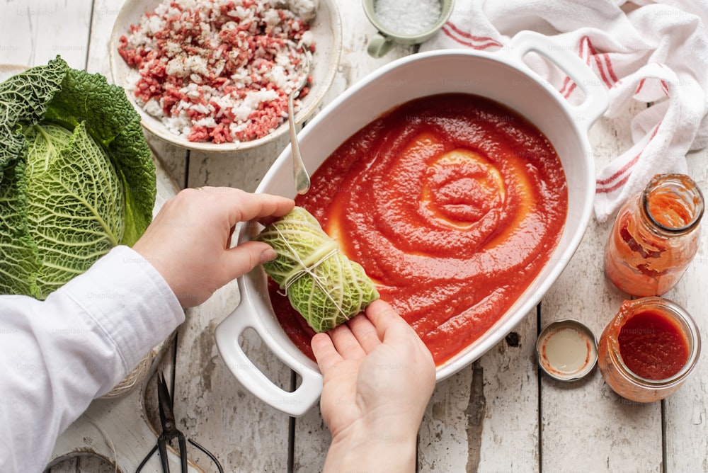 a person holding a piece of cabbage over a bowl of soup