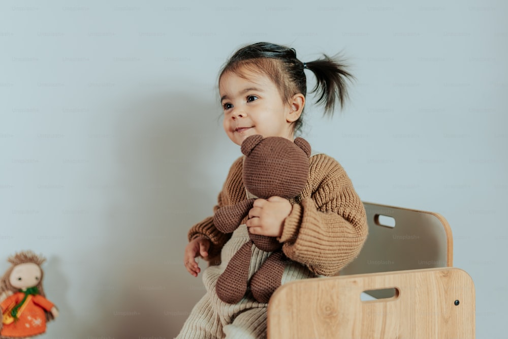 a little girl sitting on a chair holding a stuffed animal