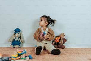 a little girl sitting on the floor with stuffed animals