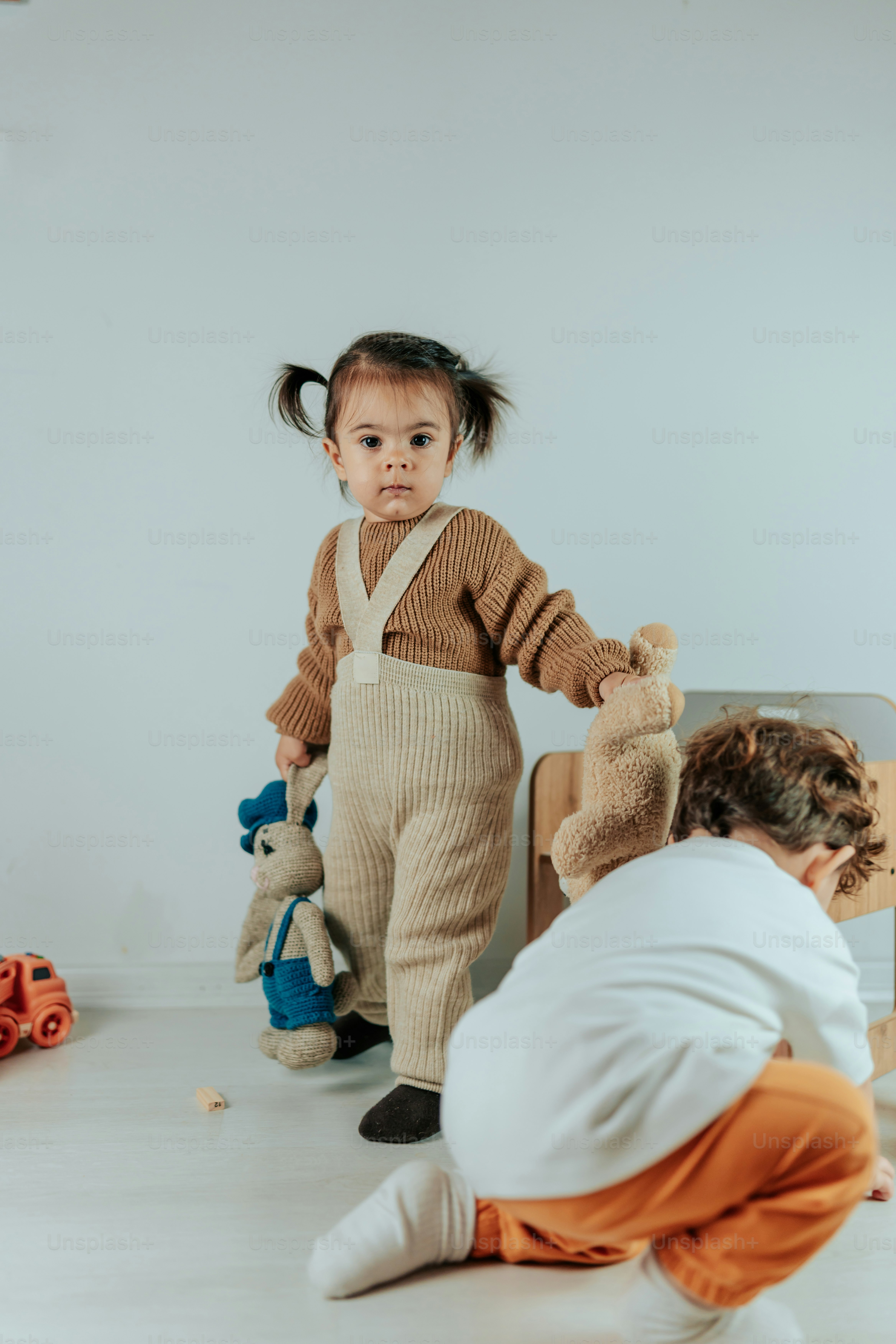 a little girl standing next to a woman holding a teddy bear