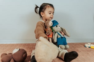 a little girl sitting on the floor with two stuffed animals