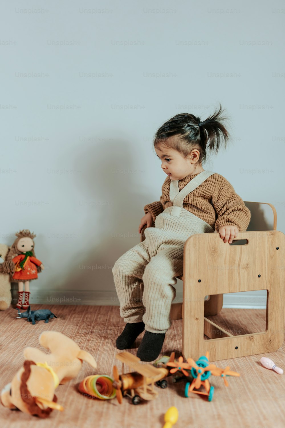 a little girl sitting in a chair with toys around her