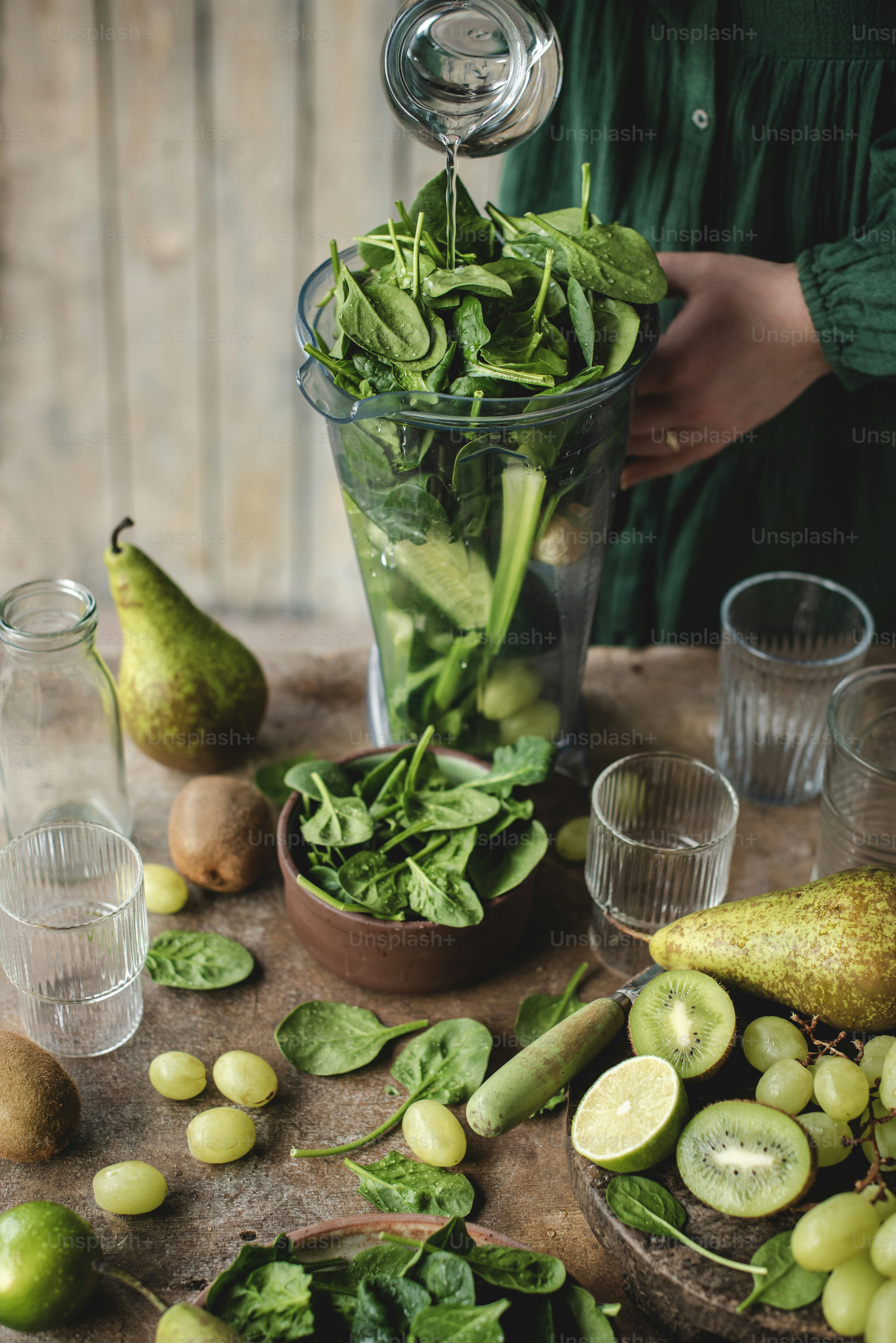 eine Person, die ein Glas mit grüner Flüssigkeit in eine Schale mit Obst gießt