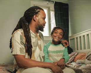 a man sitting next to a little girl on a bed