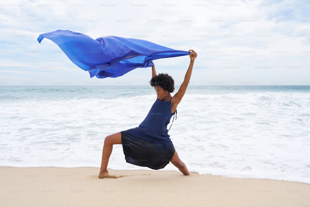 una mujer de pie en una playa sosteniendo un paño azul sobre su cabeza