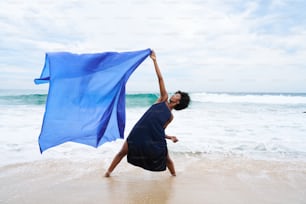 a woman holding a blue scarf on the beach
