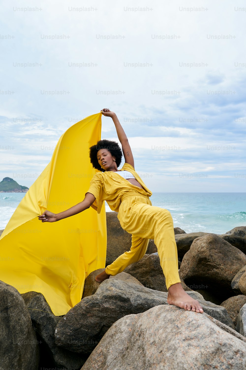 a woman in a yellow outfit standing on rocks near the ocean
