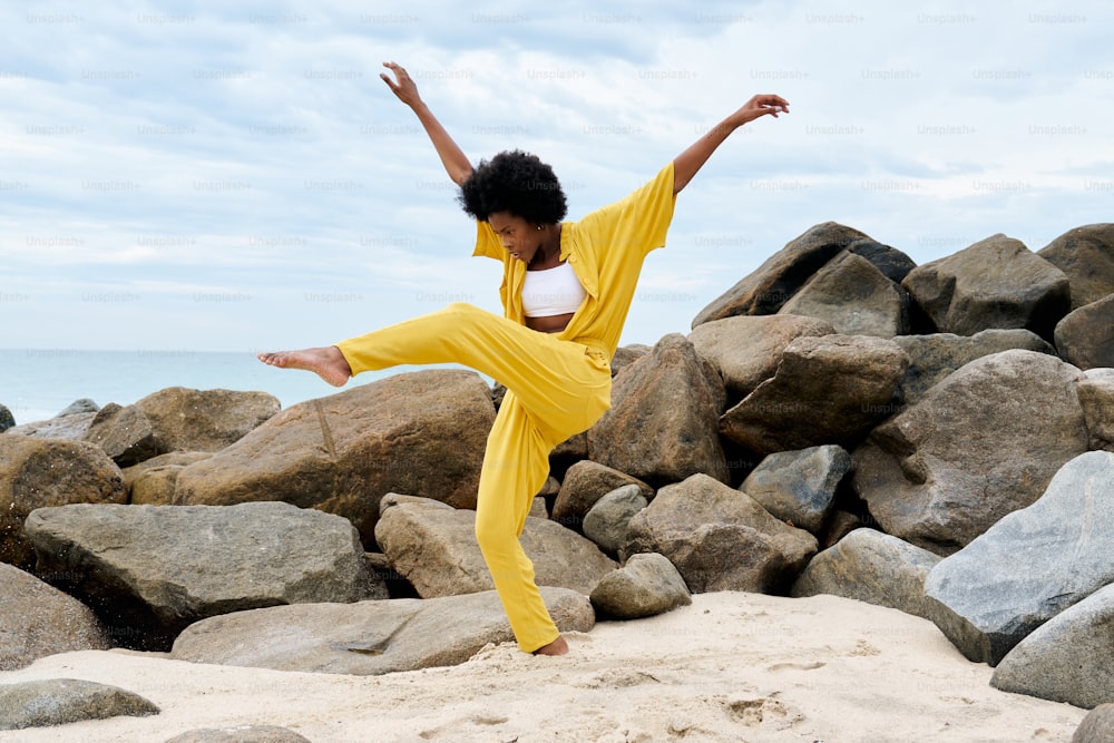 a woman in a yellow outfit doing a yoga pose on a rocky beach
