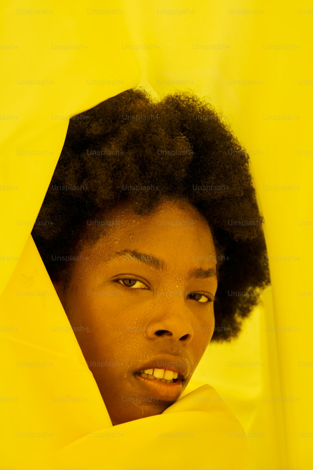 a young woman peeking out from behind a yellow curtain