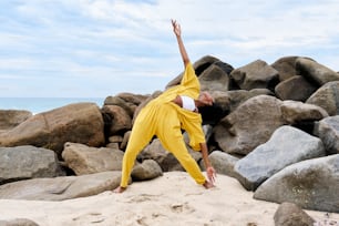 a man doing a yoga pose on a rocky beach