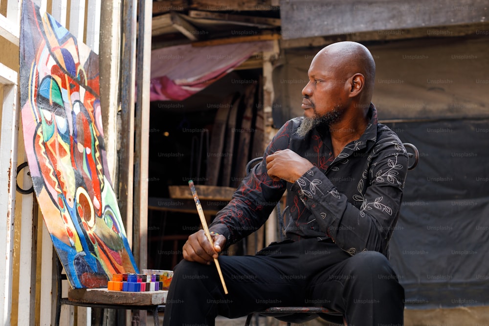 ein Mann sitzt vor einem Gemälde und hält einen Pinsel in der Hand
