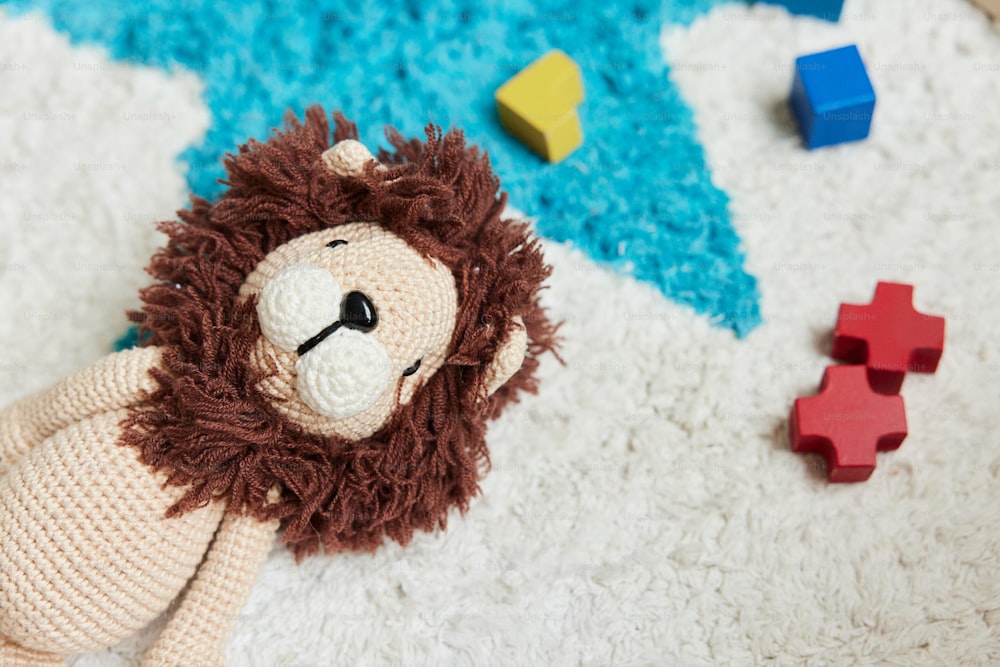 a knitted lion laying on a rug next to wooden blocks