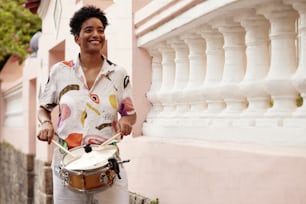 a woman standing next to a pink building holding a drum