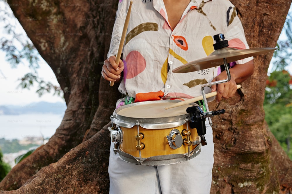 a man holding a drum in front of a tree