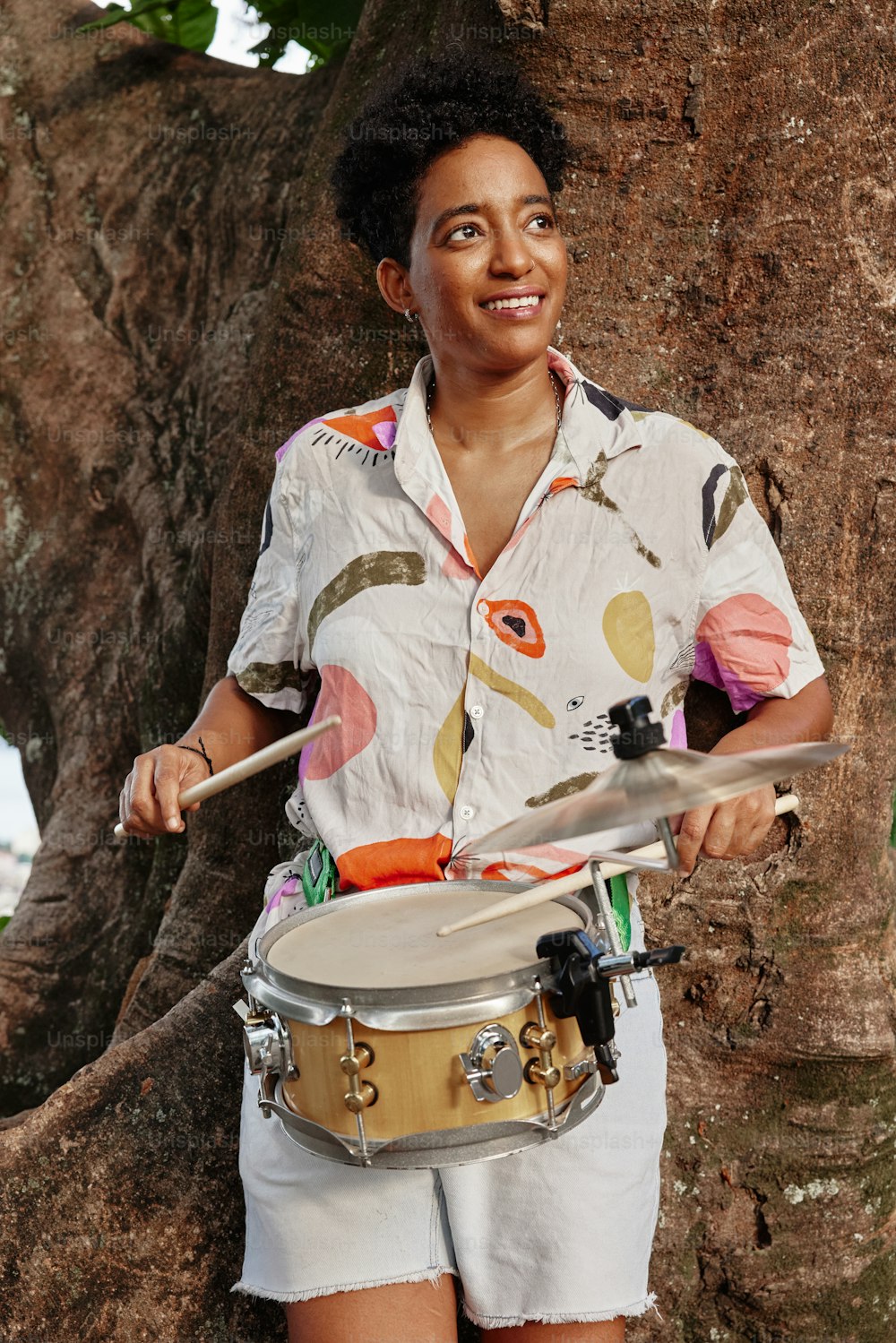 uma mulher segurando um tambor na frente de uma árvore