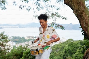 a woman holding a drum on top of a lush green hillside