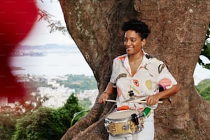 a woman standing next to a tree holding a drum